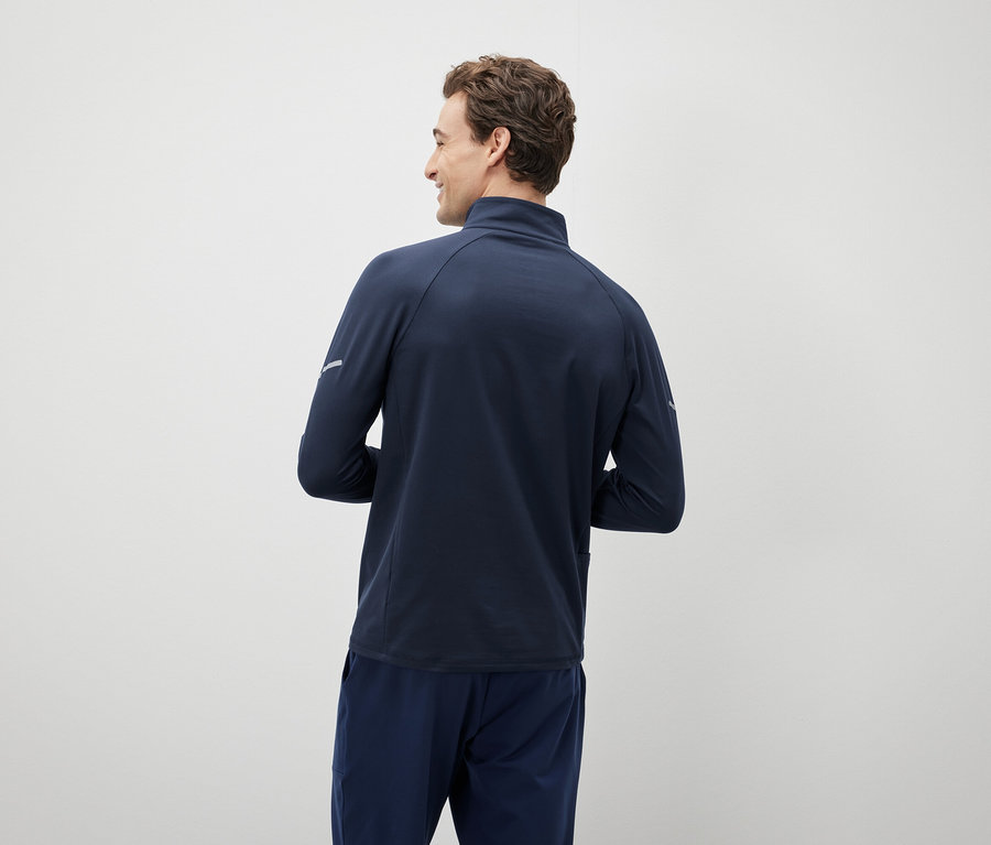 Mężczyzna patrzy przez ramię, ubrany w granatową kurtkę i spodnie.