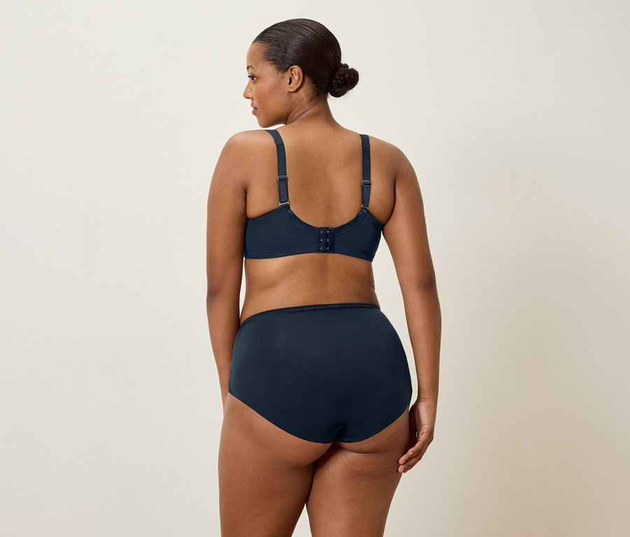 Kobieta o ciemnych włosach, widziana od tyłu, ma na sobie granatowy biustonosz i pasujące majtki.