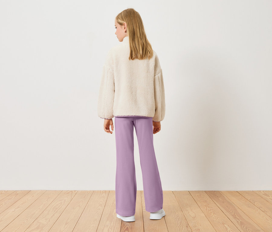 Widok z tyłu na blondynkę w kremowej bluzie z polaru typu teddy i liliowych spodniach.