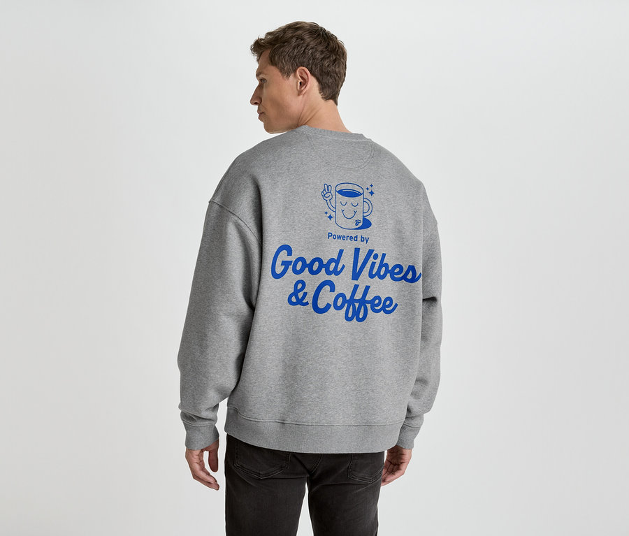 Mężczyzna od tyłu w szarej bluzie z niebieskim nadrukiem 'Good Vibes & Coffee'.