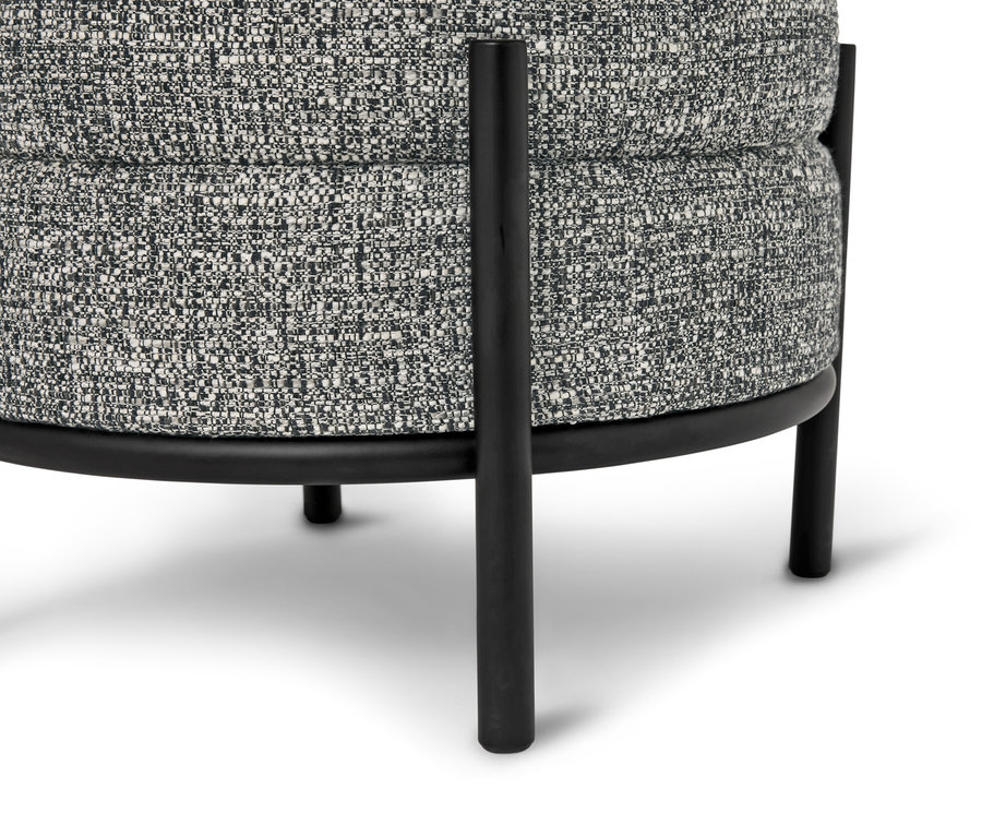 Zbliżenie okrągłego stołka z szarą, wzorzystą tapicerką i czarnymi metalowymi nogami.