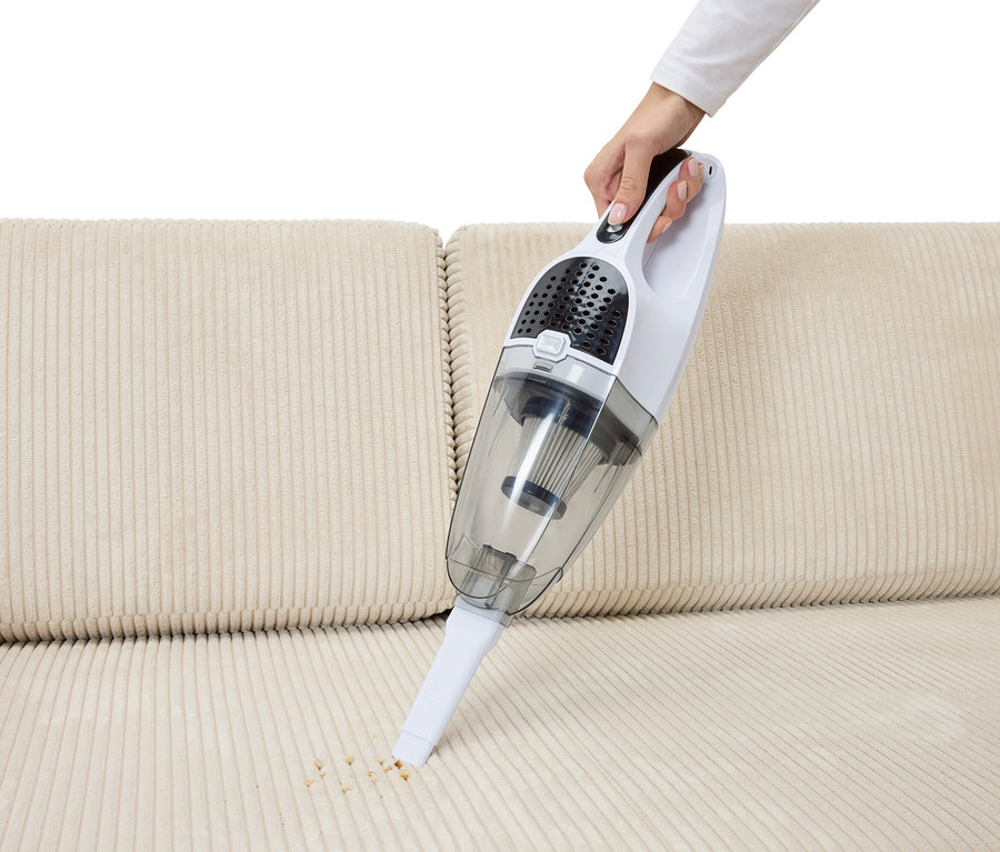 Ręka odkurza okruchy 2-w-1 odkurzaczem akumulatorowym z beżowej sofy.