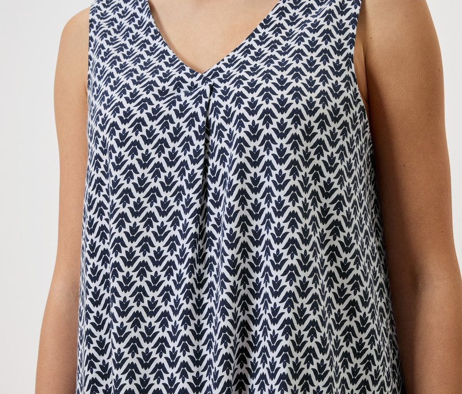 Zbliżenie kobiety w bezrękawnikowej sukience we wzory w kolorze biało-niebieskim.