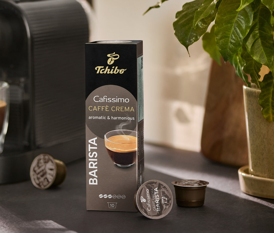 Ekspres do kawy napełnia szklankę kawą. Obok stoi opakowanie Cafissimo BARISTA Caffè Crema i kilka kapsułek.