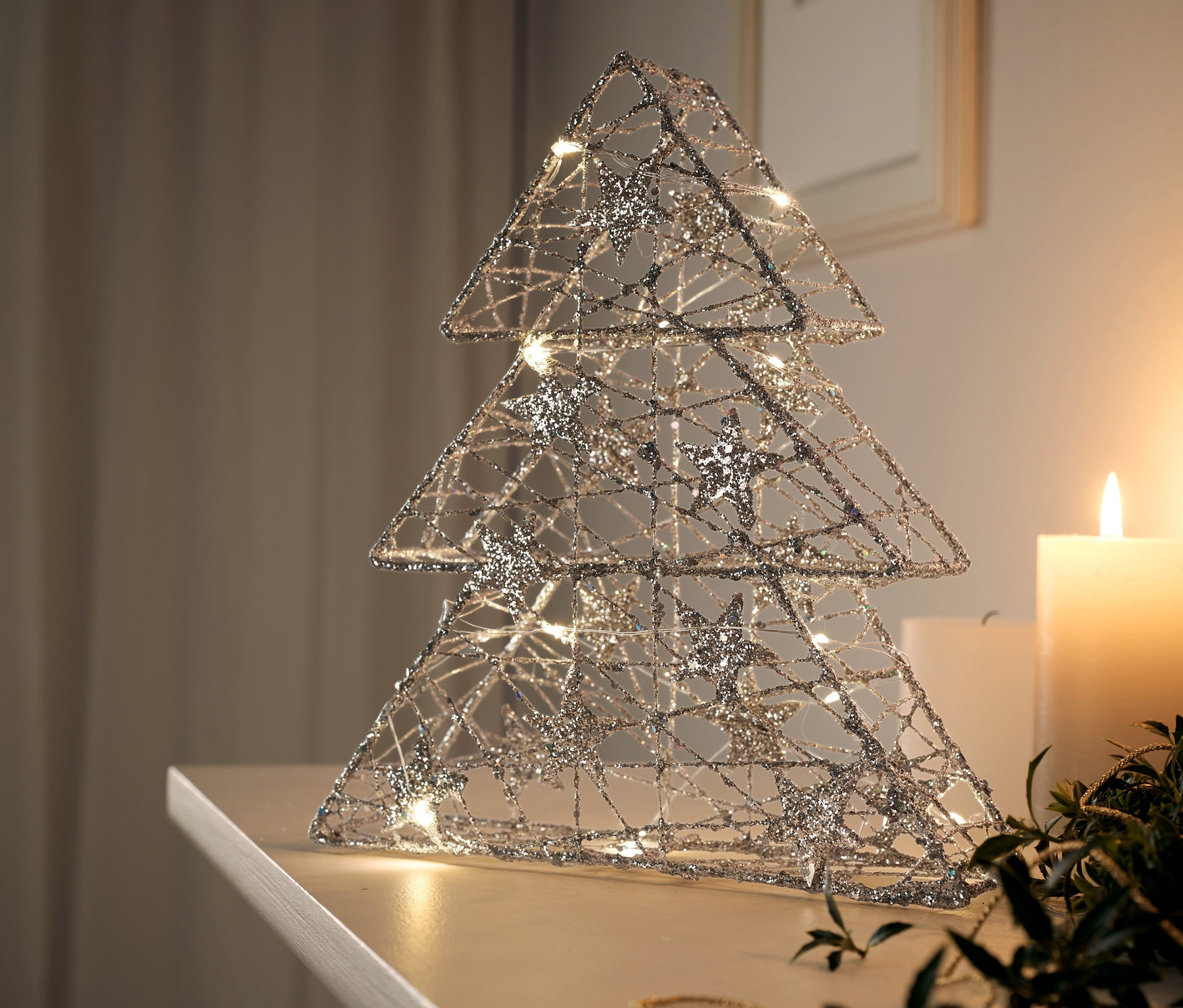 Złota choinka LED stoi na białej półce obok zapalonej świecy.
