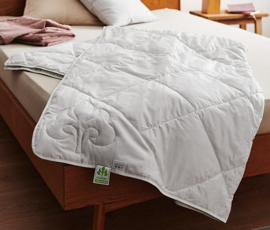 Na łóżku leży biała letnia kołdra pikowana irisette® greenline z bawełny z lnem.