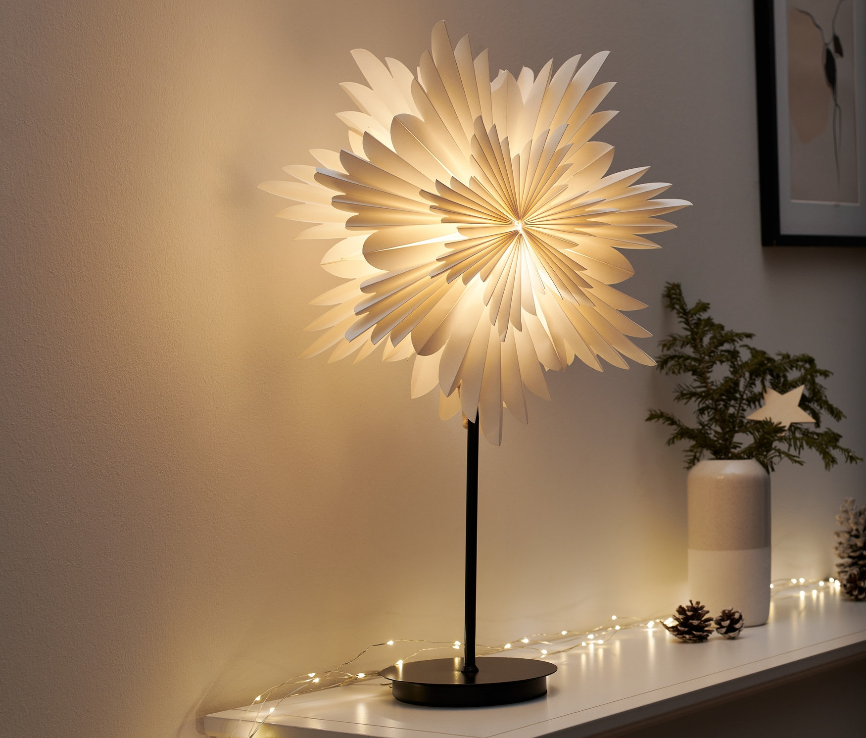 Lampa dekoracyjna LED »gwiazda« stoi na białej półce. Wokół niej znajdują się łańcuchy świetlne i dekoracje świąteczne.