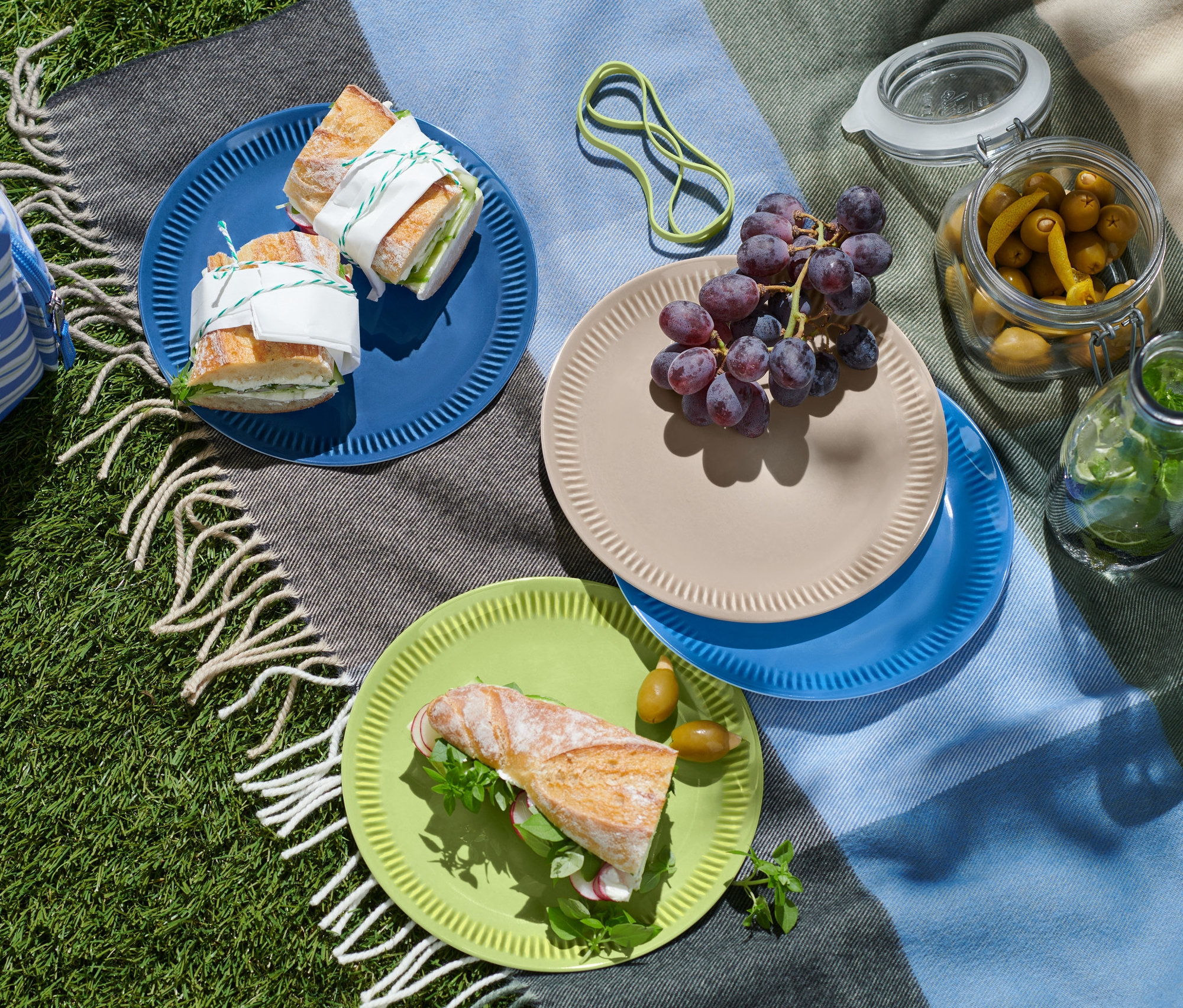 Kanapki na talerzach piknikowych, napoje w torbie chłodzącej i oliwki w pojemniku na kocu.