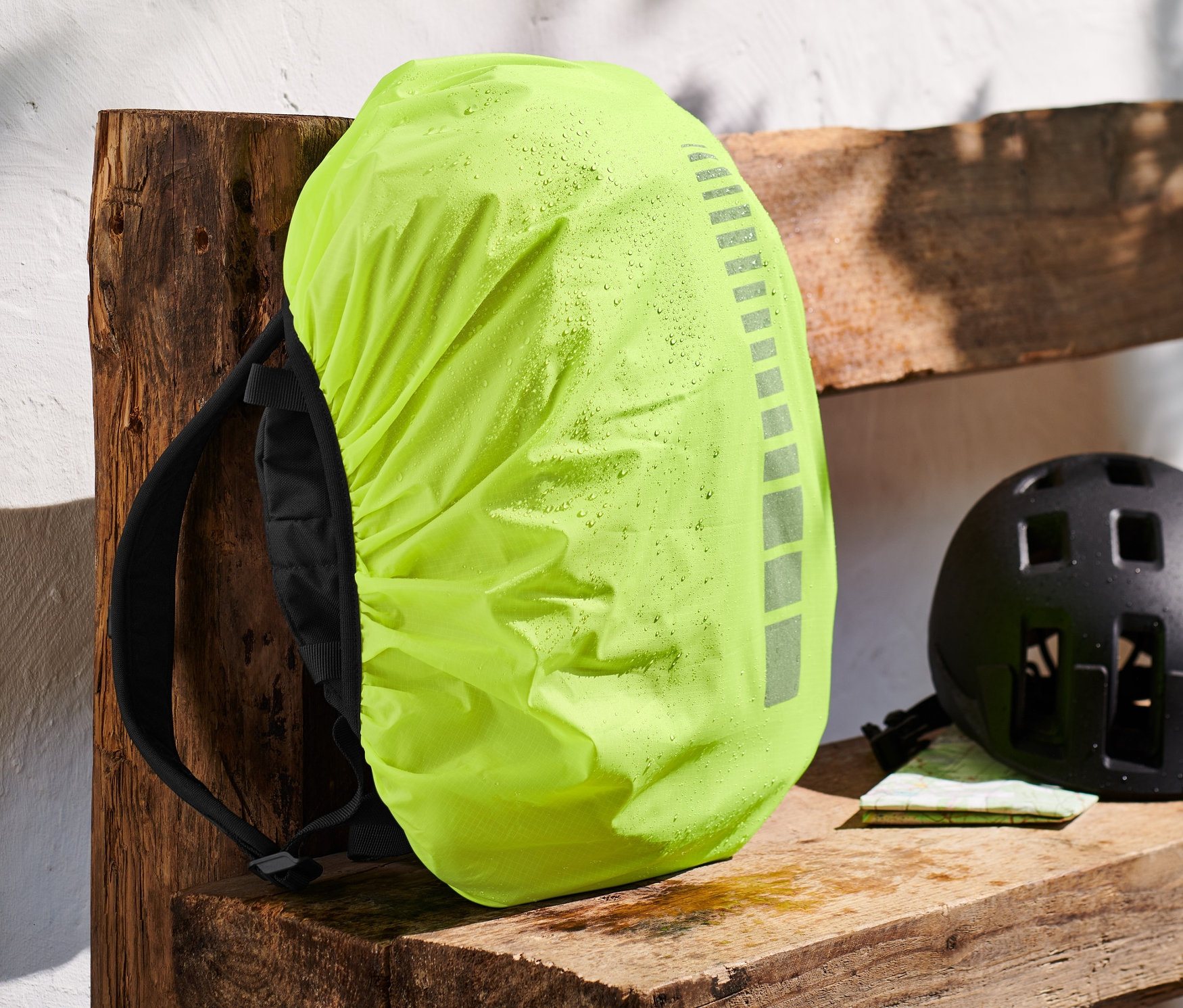 Plecak z pokrowcem przeciwdeszczowym na plecak leży na drewnianej ławce.