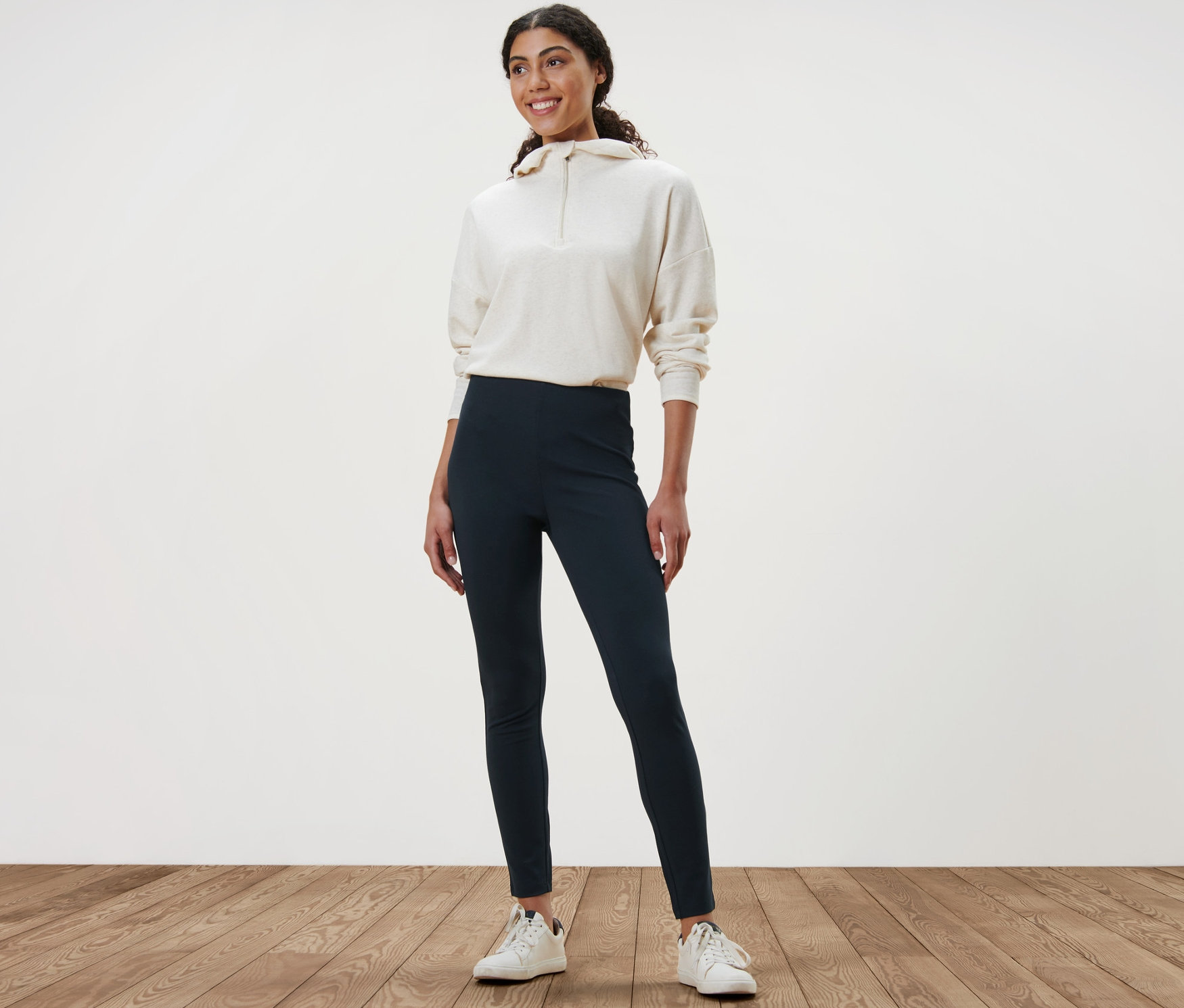 Kobieta stojąca na drewnianej podłodze ma na sobie grube legginsy i bluzę.