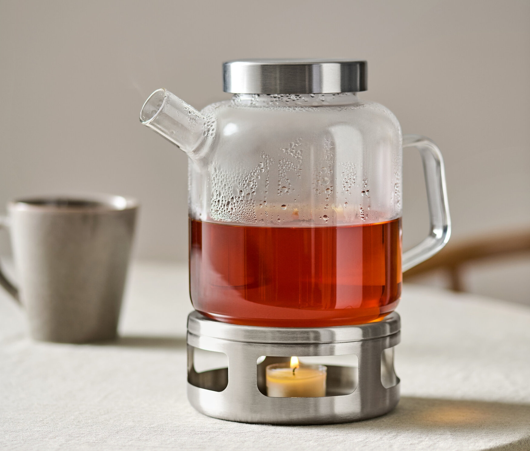 Szklany czajnik z herbatą stoi na podgrzewaczu ze świecą.