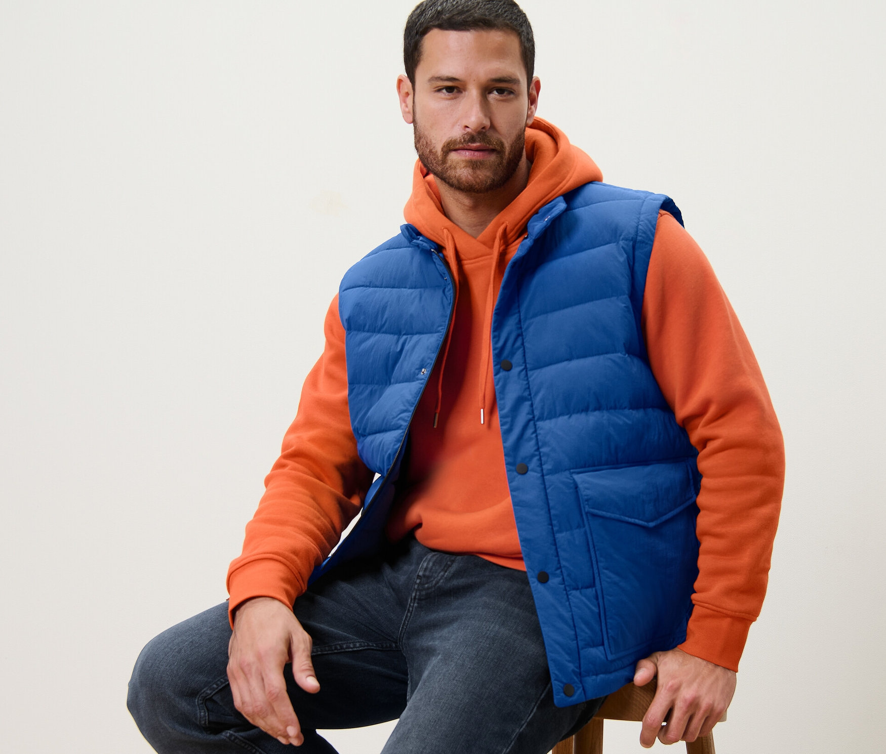 Mężczyzna siedzi na stołku w niebieskiej kamizelce pikowanej.