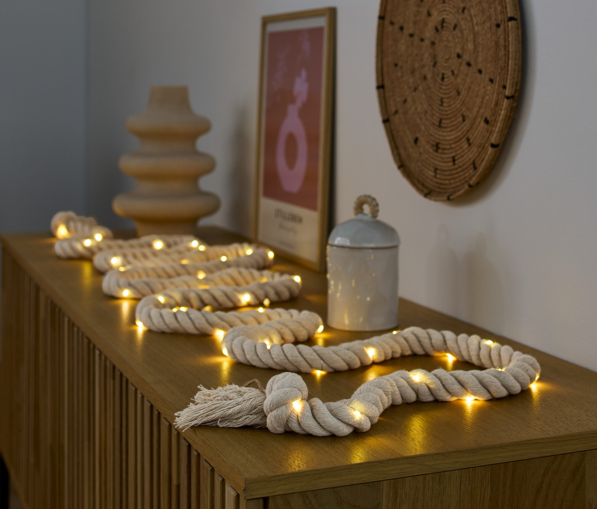 Łańcuch świetlny LED „Lina” leży na drewnianej komodzie obok wazonu i puszki.