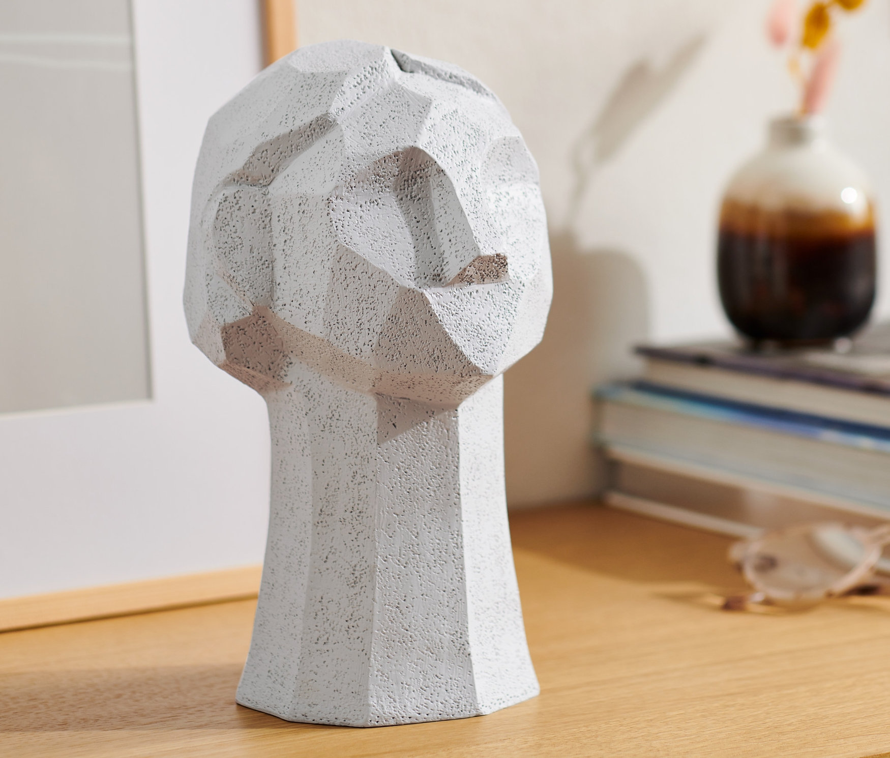 Szara rzeźba dekoracyjna w kształcie głowy na drewnianym stole.