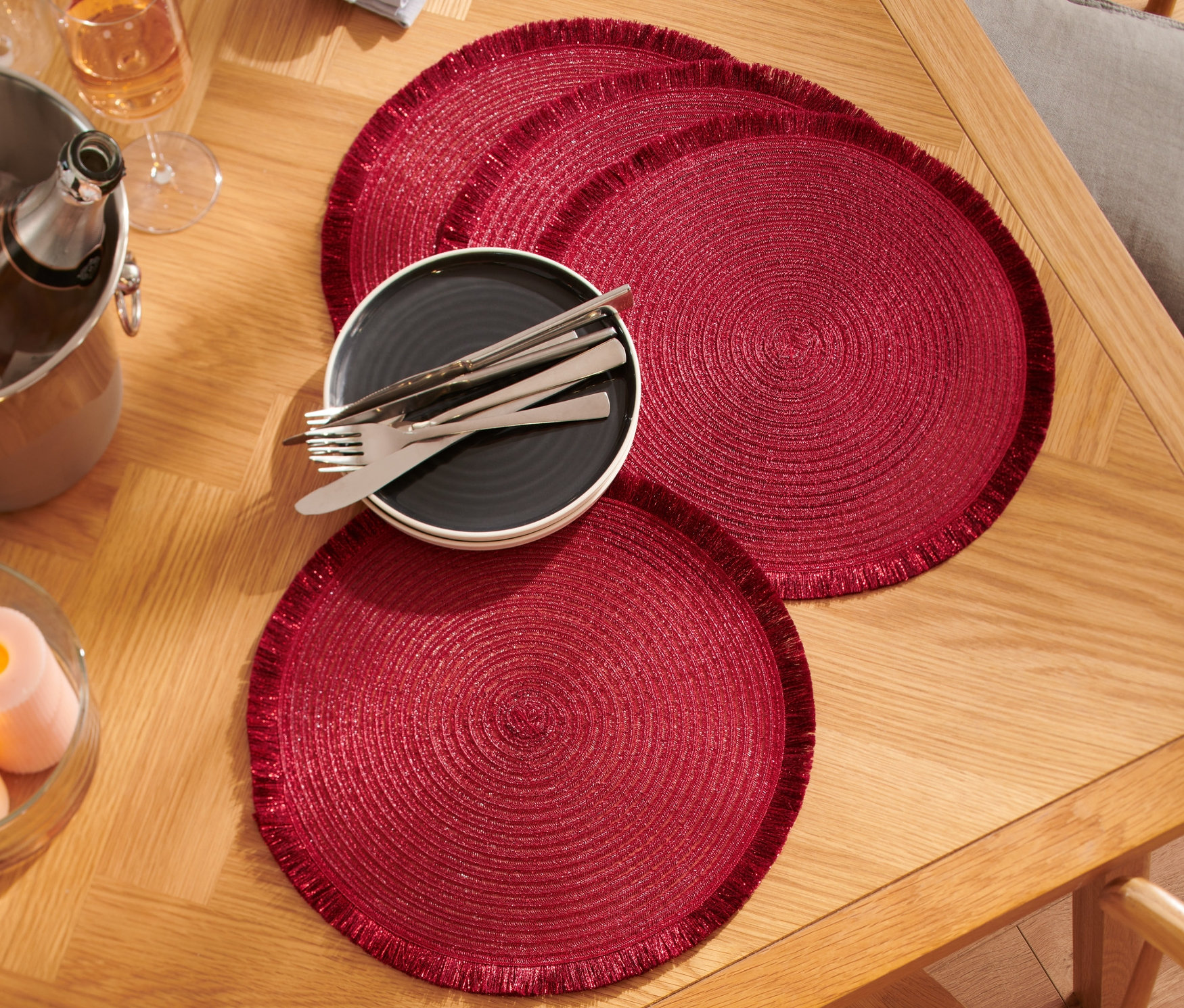 Cztery czerwone podkładki pod talerze na drewnianym stole z talerzem, sztućcami, szklankami i wiaderkiem do szampana.