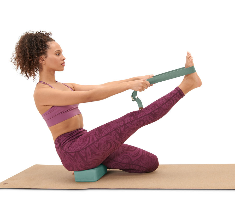 Kobieta siedzi na macie do jogi z blokiem do jogi i używa paska do jogi z zestawu do jogi.