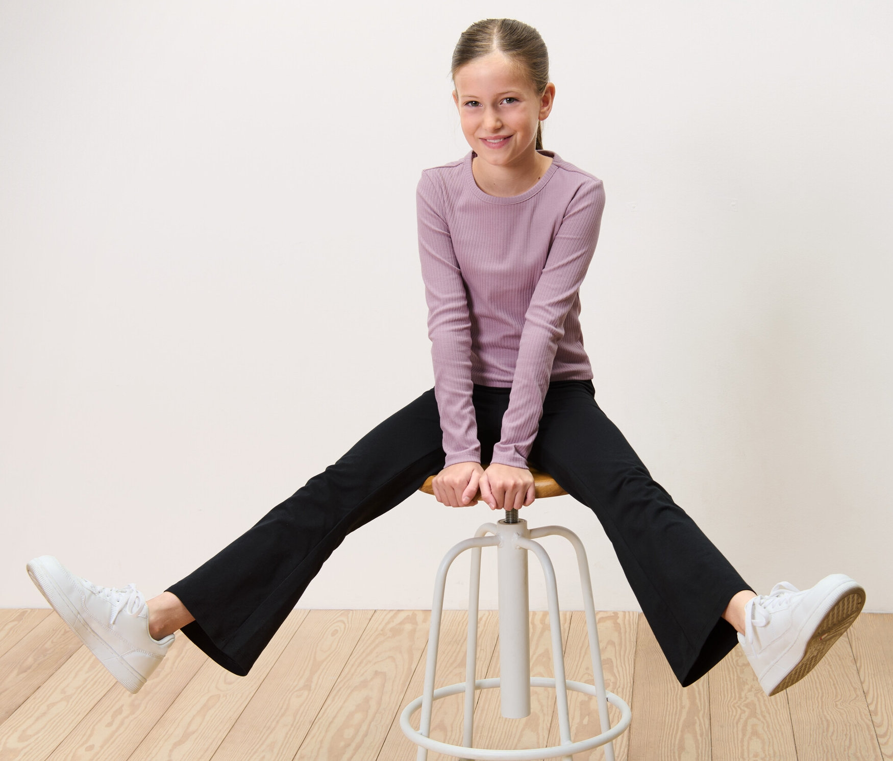 Dziewczyna siedzi okrakiem na stołku i ma na sobie rozszerzane legginsy, 2 pary.