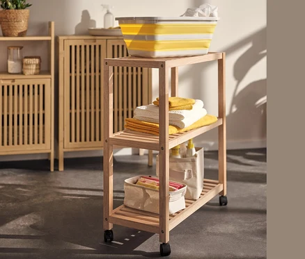 Żółty składany kosz na pranie na regale z litego drewna z kółkami obok szafki typu sideboard.