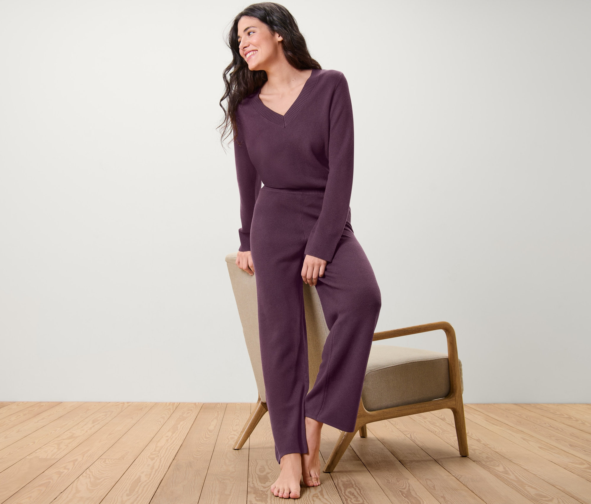 Kobieta opiera się o krzesło, ma na sobie fioletowe spodnie rekreacyjne z dzianiny.