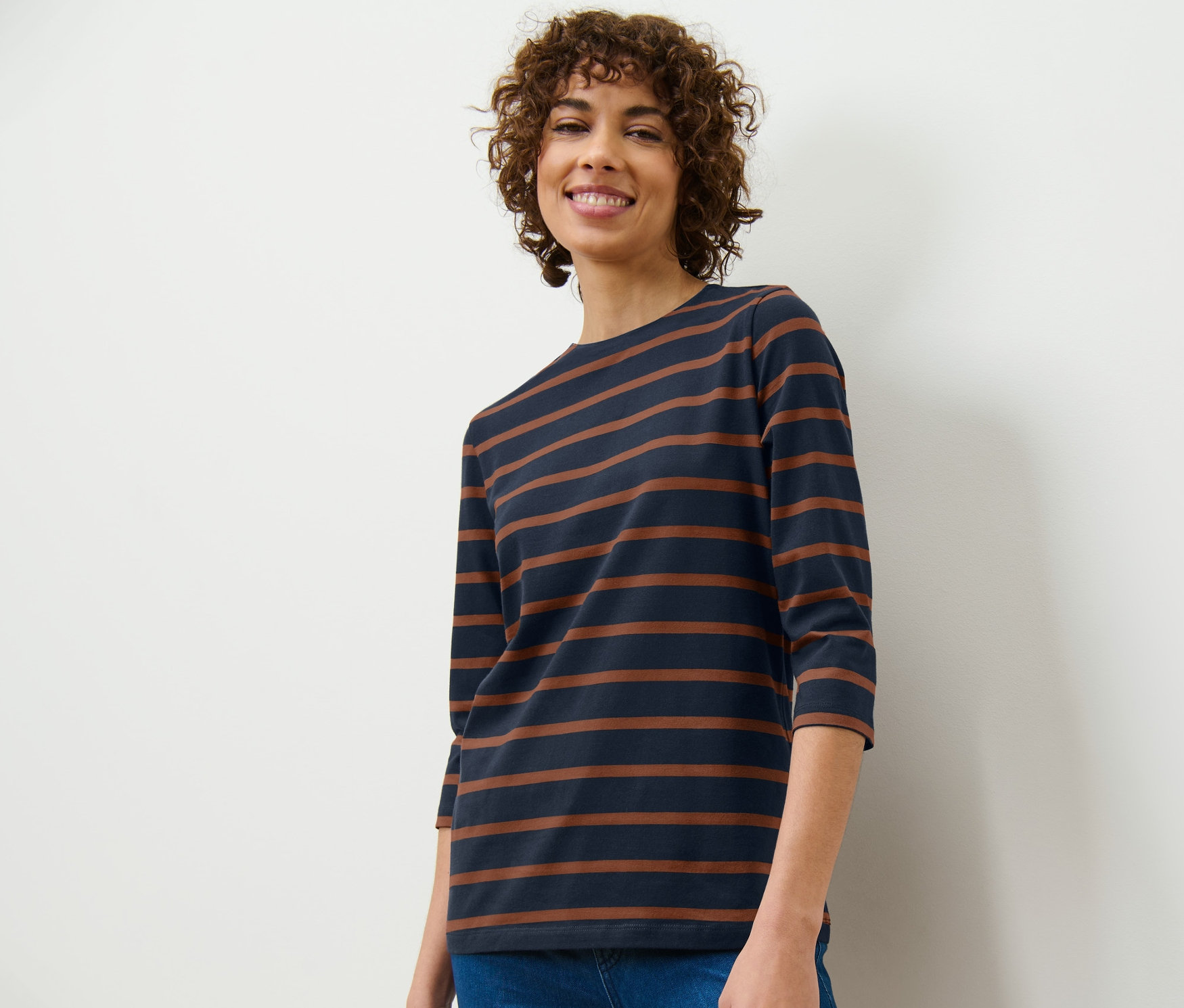 Kobieta ma na sobie bluzkę z rękawami o długości 3/4 w paski i dżinsy.