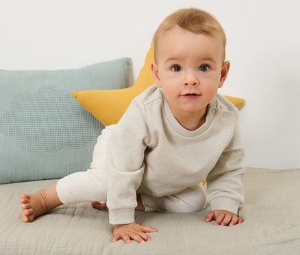 Dziecko raczkuje po macie obok poduszek. Ma na sobie bluzy niemowlęce z drapaną stroną wewnętrzną, 2 sztuki.