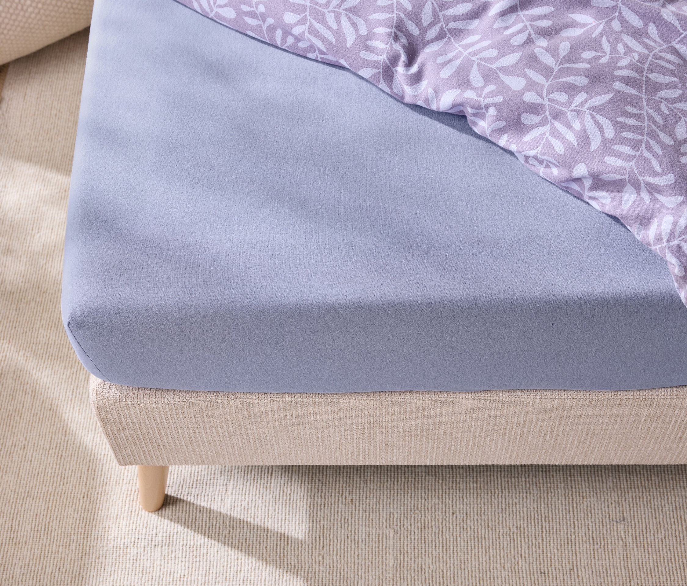 Szczegół łóżka z niebieskim prześcieradłem z gumką i pościelą w liście.