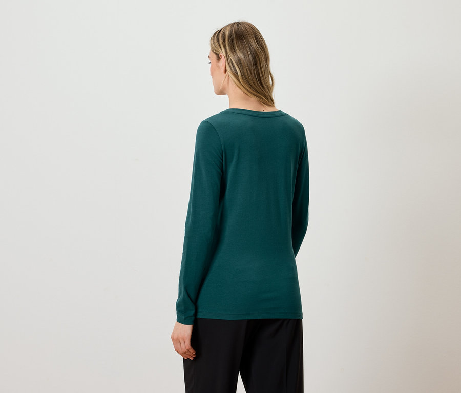 Z tyłu widać kobietę z blond włosami, ubraną w zieloną bluzkę z długim rękawem i czarne spodnie.