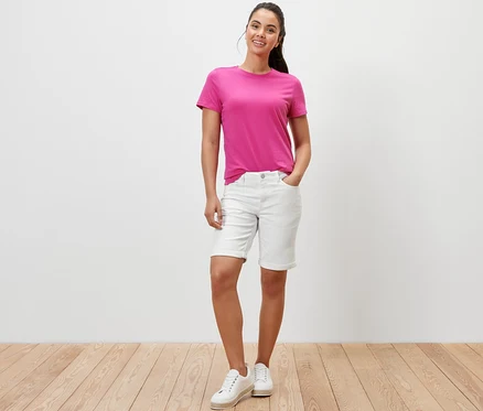 Kobieta pozuje w kremowych szortach jeansowych ‒ krój „Lea” i różowym T-shircie.