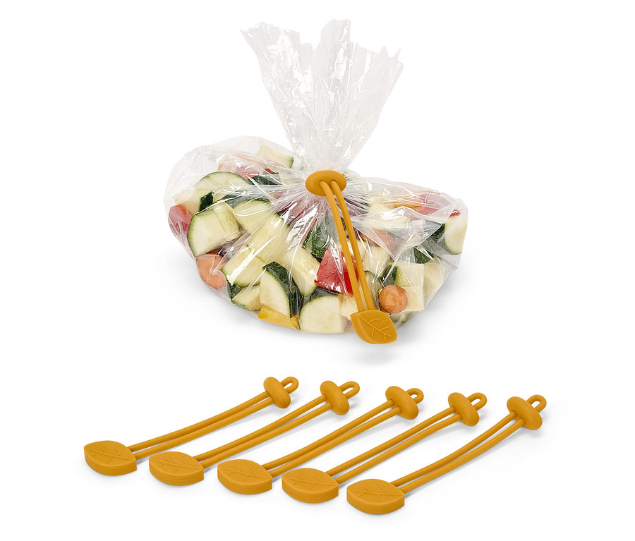 Kostki cukinii, marchwi i papryki w plastikowym worku, zamkniętym żółtą silikonową opaską zaciskową z motywem liścia. Pod workiem znajdują się cztery żółte silikonowe opaski.