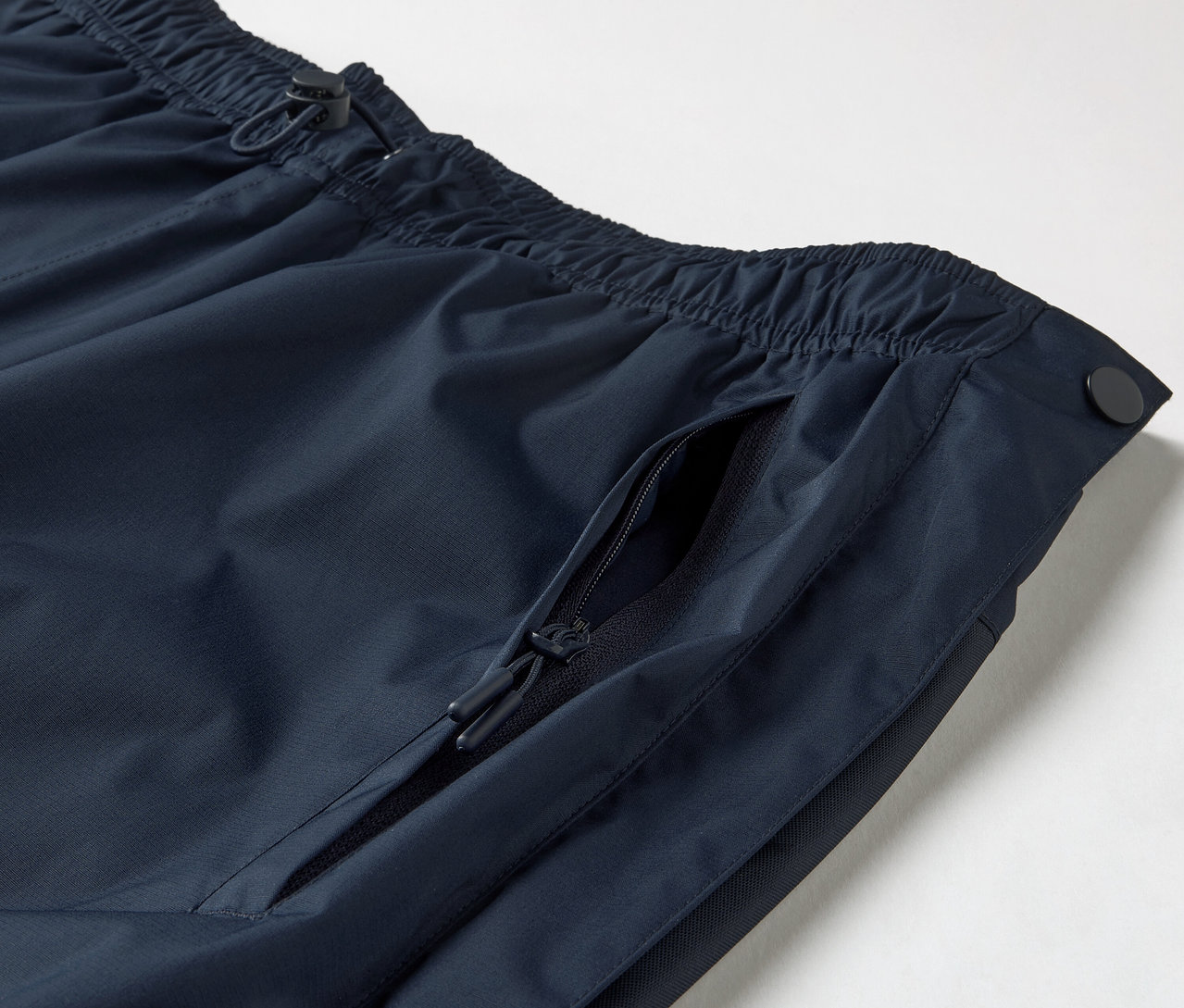 Zbliżenie na spodnie przeciwdeszczowe z zamkiem błyskawicznym na całej długości, pokazujące elastyczny pas ze sznurkiem i kieszeń na zamek błyskawiczny.