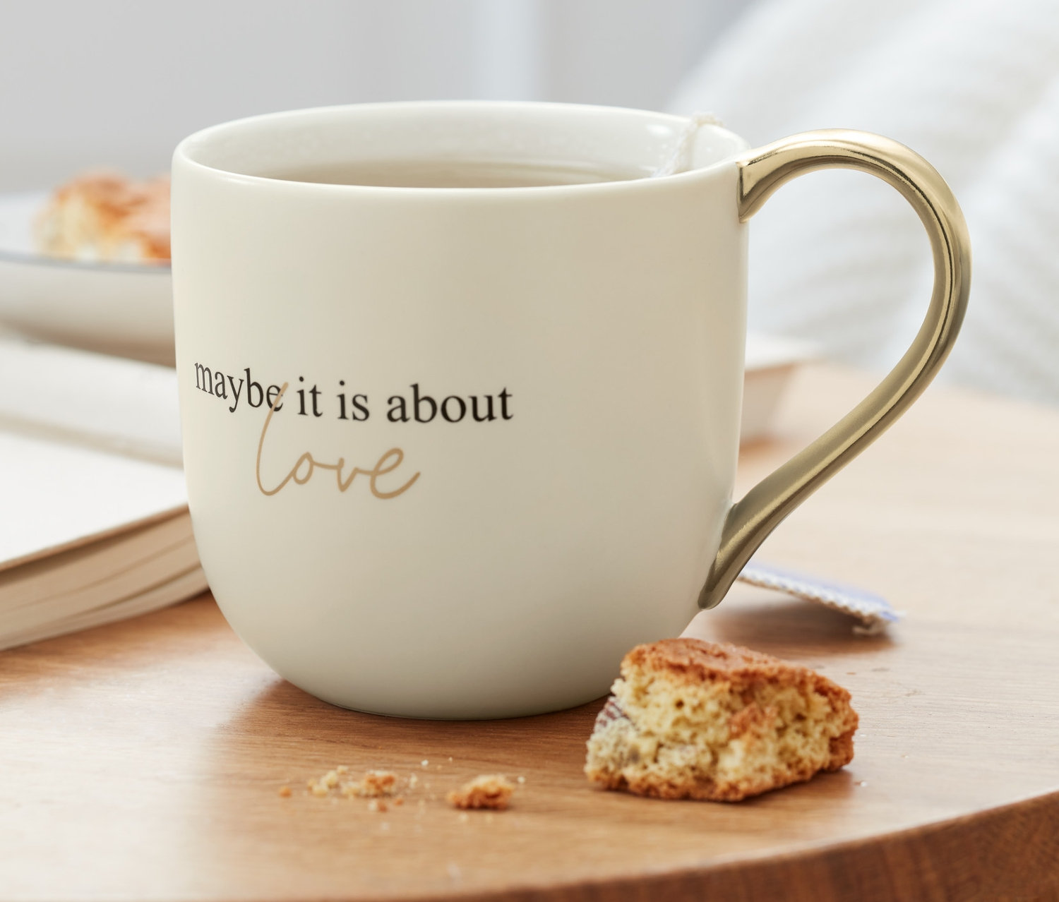 Na drewnianym stoliku stoi filiżanka z napisem i kawałek ciastka.