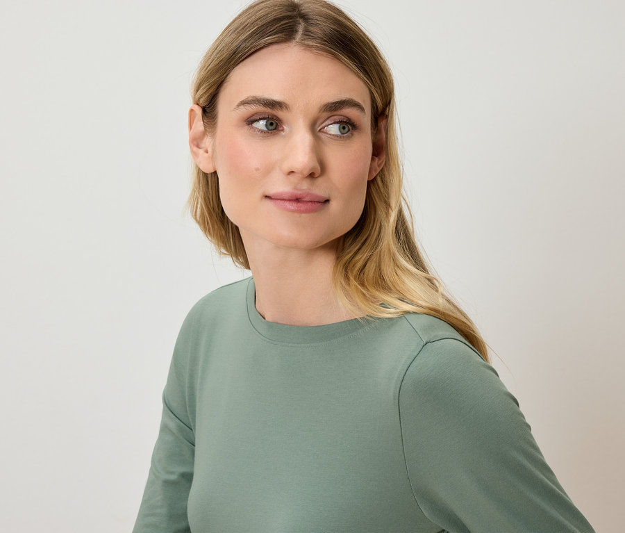 Portret kobiety z blond włosami w zielonej koszulce z długim rękawem.