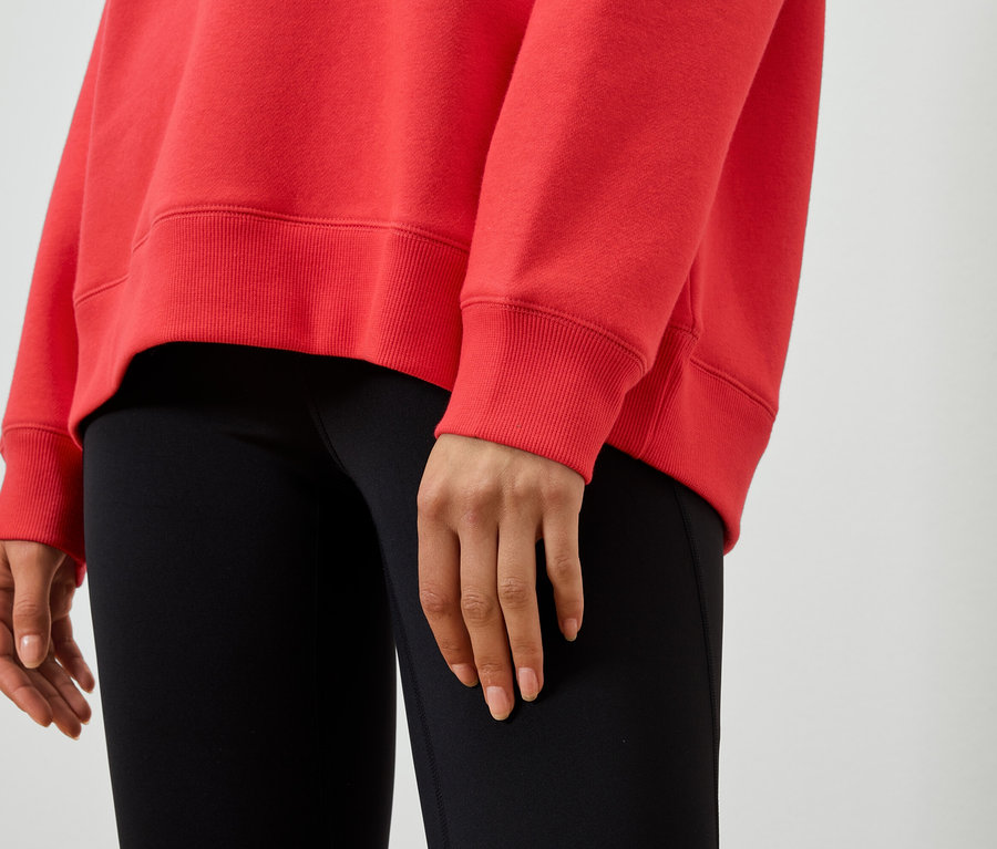 Zbliżenie na kobietę w czerwonej bluzie i czarnych legginsach.