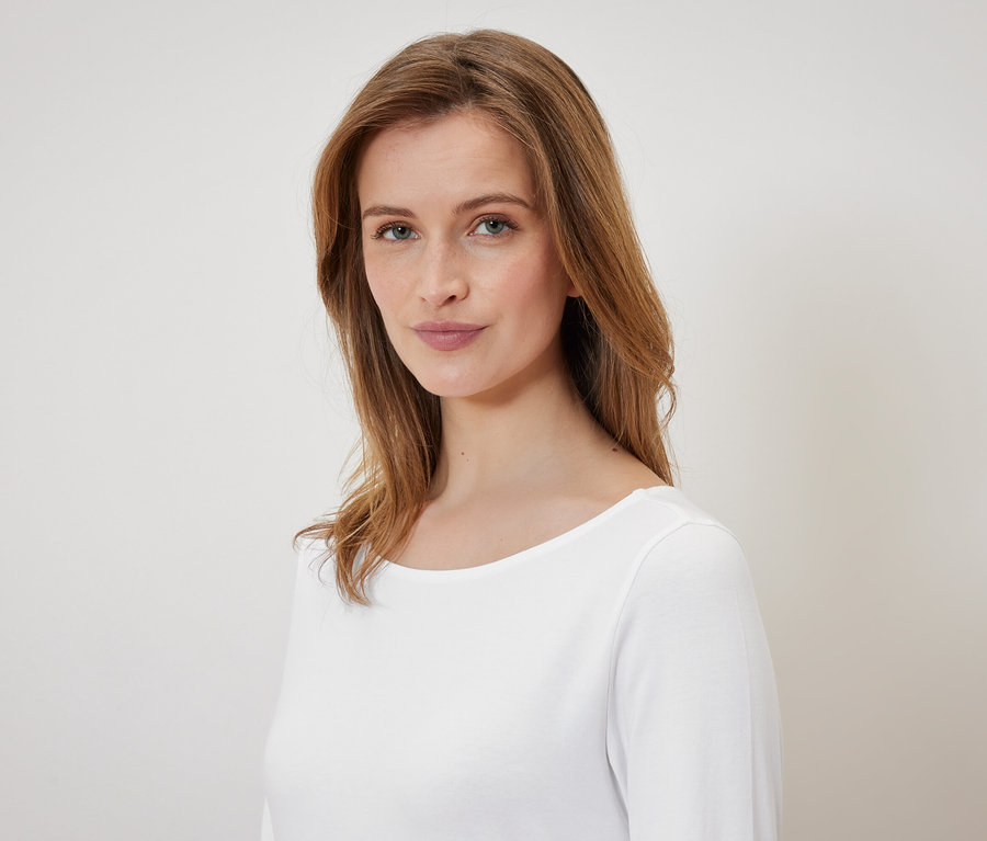 Portret kobiety z brązowymi włosami i niebieskimi oczami w białym t-shircie.