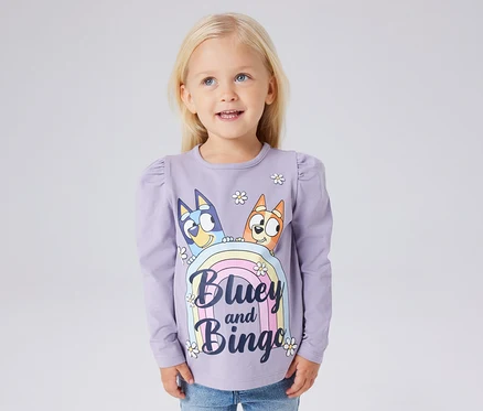 Dziewczynka ma na sobie liliową koszulkę z długim rękawem NAME IT „BLUEY” z nadrukiem Bluey i Bingo.