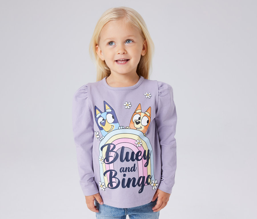 Dziewczynka ma na sobie liliową koszulkę z długim rękawem NAME IT „BLUEY” z nadrukiem Bluey i Bingo.