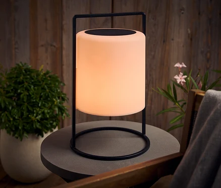 Świecąca lampa z czarną ramą stoi na szarym stole na zewnątrz.