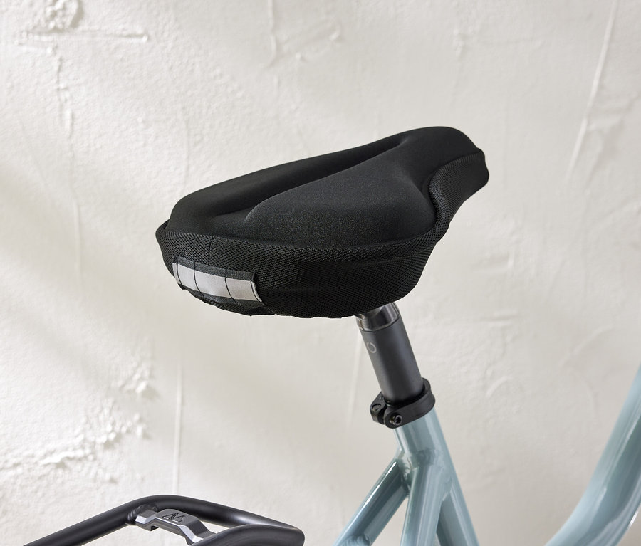 Zbliżenie siodełka rowerowego z czarnym pokrowcem i paskami odblaskowymi na tle białej ściany.