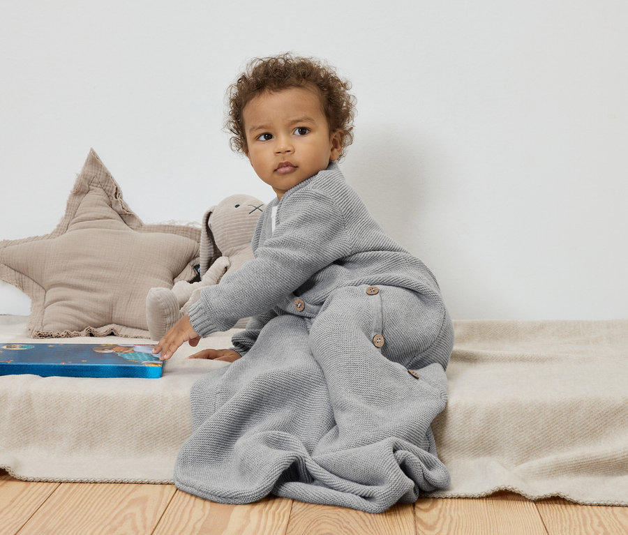 Dziecko siedzi na beżowym kocu obok pluszowej gwiazdy i królika, dotykając niebieskiej książki.