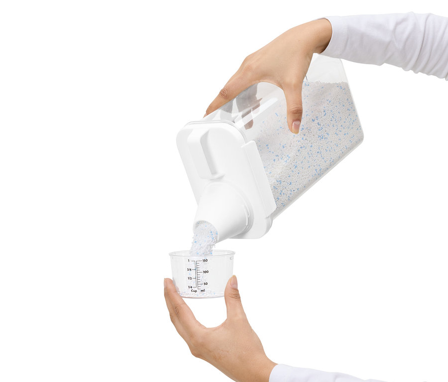 Osoba przesypuje detergent z przezroczystego pojemnika do miarki.