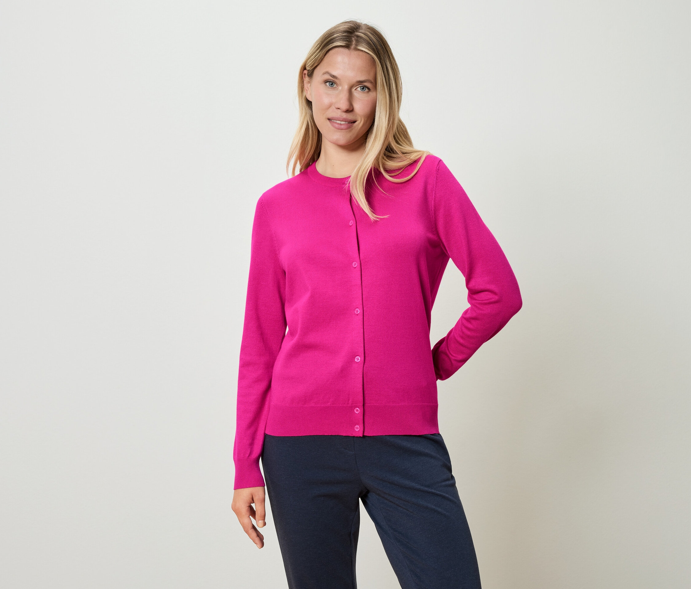 Kobieta ma na sobie różowy kardigan i niebieskie spodnie.