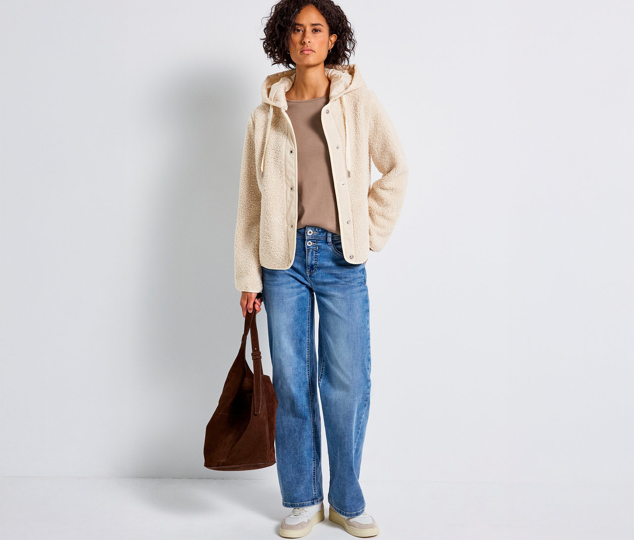 Kobieta ma na sobie pluszową bluzę z odpinanym kapturem od Street One, dżinsy i trzyma brązową torbę.