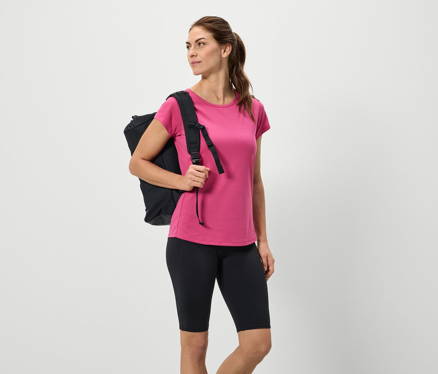 Kobieta z czarnym plecakiem, różową koszulką i czarnymi szortami.