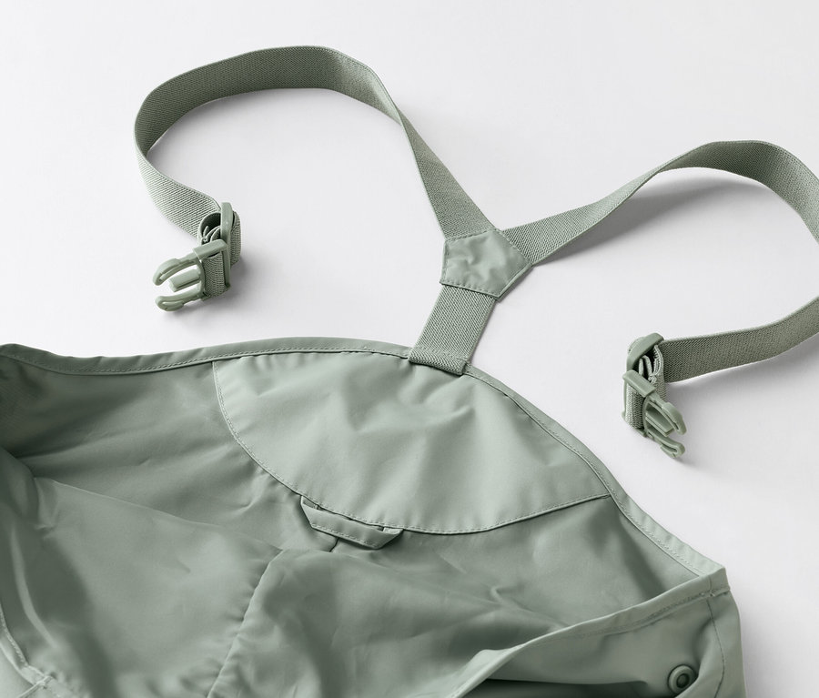Zbliżenie na zielone spodnie przeciwdeszczowe na szelkach z klamrami na białym tle.