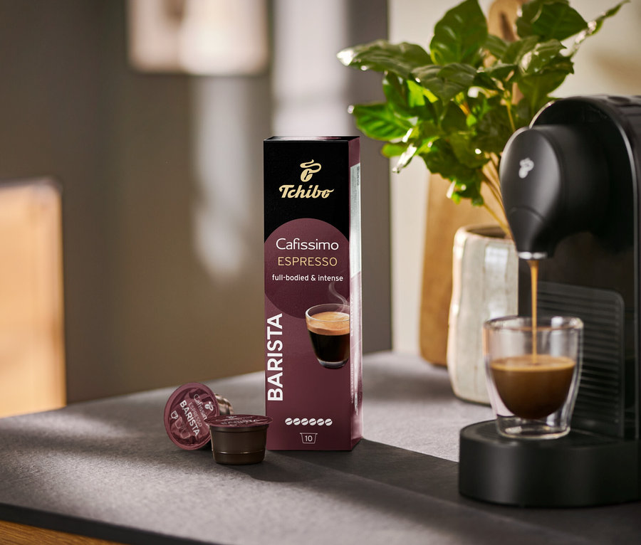 Espresso wlewa się do szklanki z ekspresu Cafissimo BARISTA, obok opakowanie 10 kapsułek.