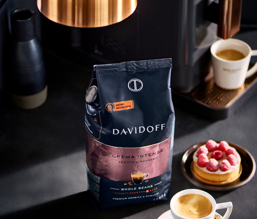 Opakowanie DAVIDOFF CAFÉ Crema Intense 1000 g ziarna stoi obok filiżanki kawy i ciasta malinowego.