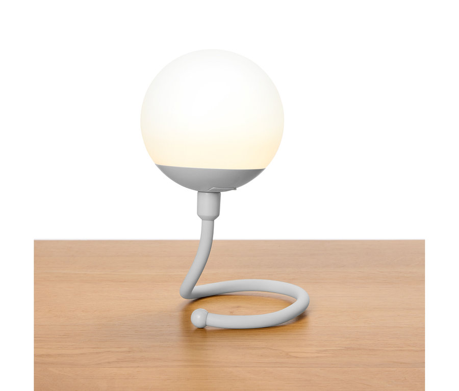 Szara, kulista lampa ze zakrzywioną szyjką stoi na drewnianym stole.