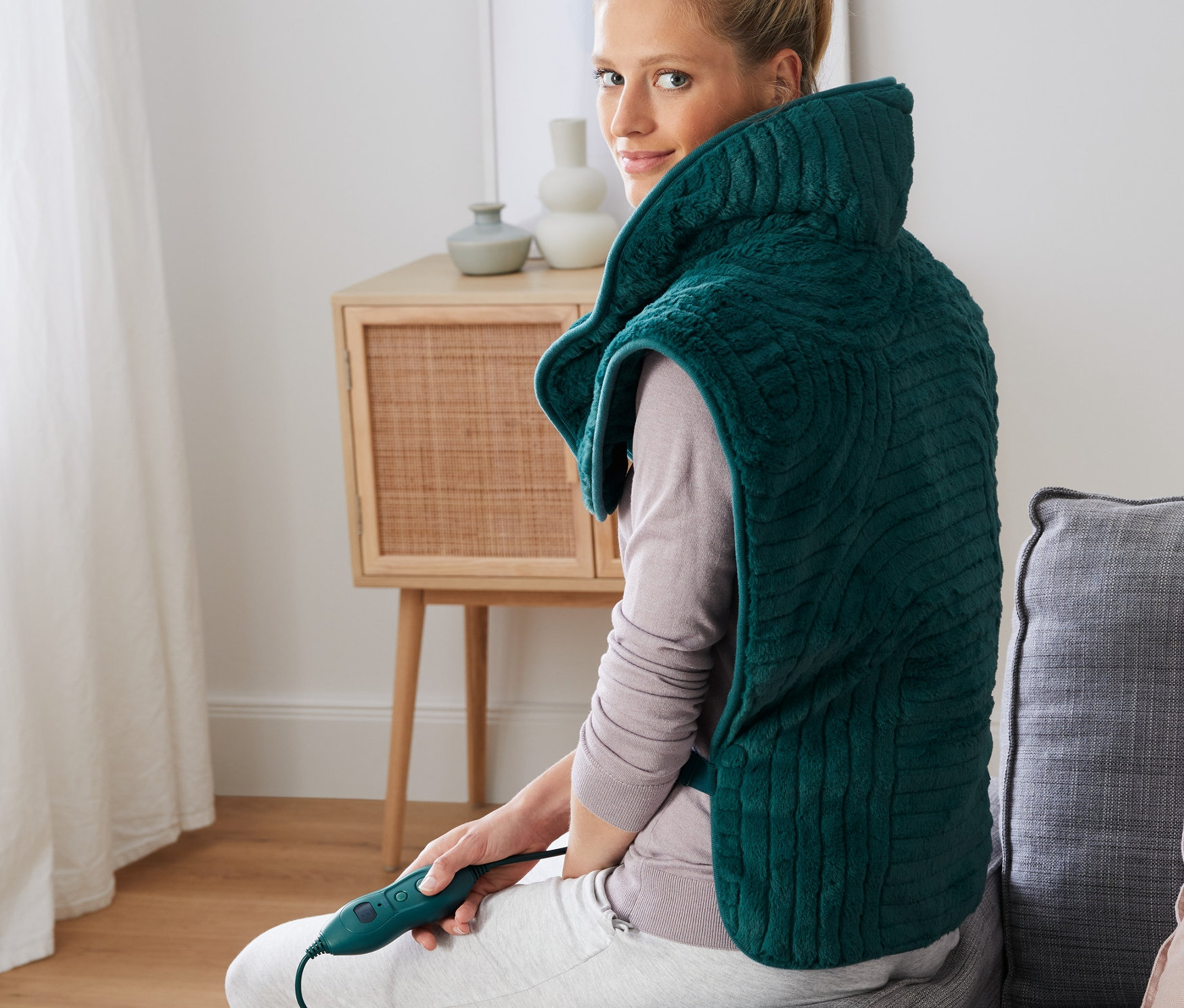 Kobieta siedzi na kanapie z poduszką elektryczną na plecy.