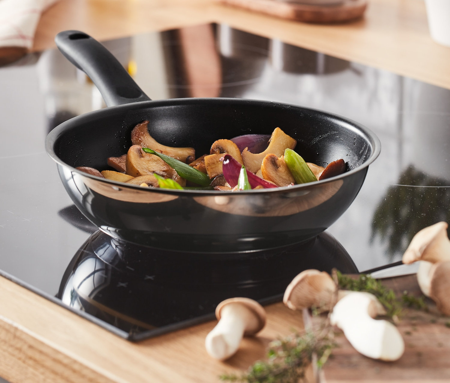 Na płycie grzewczej stoi patelnia ze stali nierdzewnej o średnicy ok. 20 cm, na której smażone są warzywa.