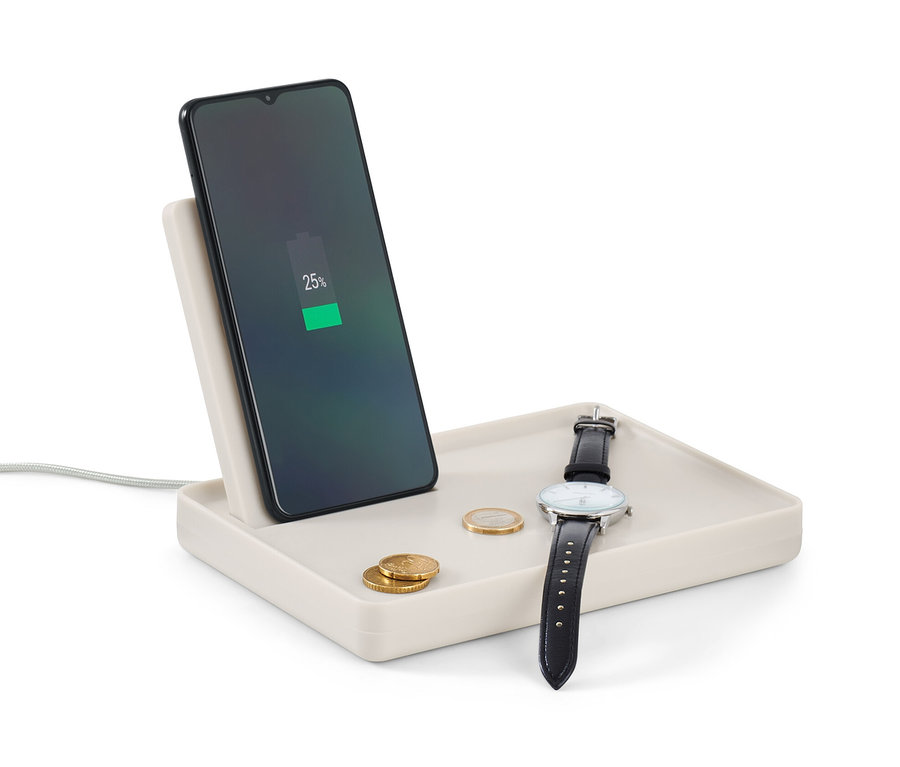 Telefon ładuje się na podstawce do ładowania smartfona. Na podstawce leżą zegarek i monety.
